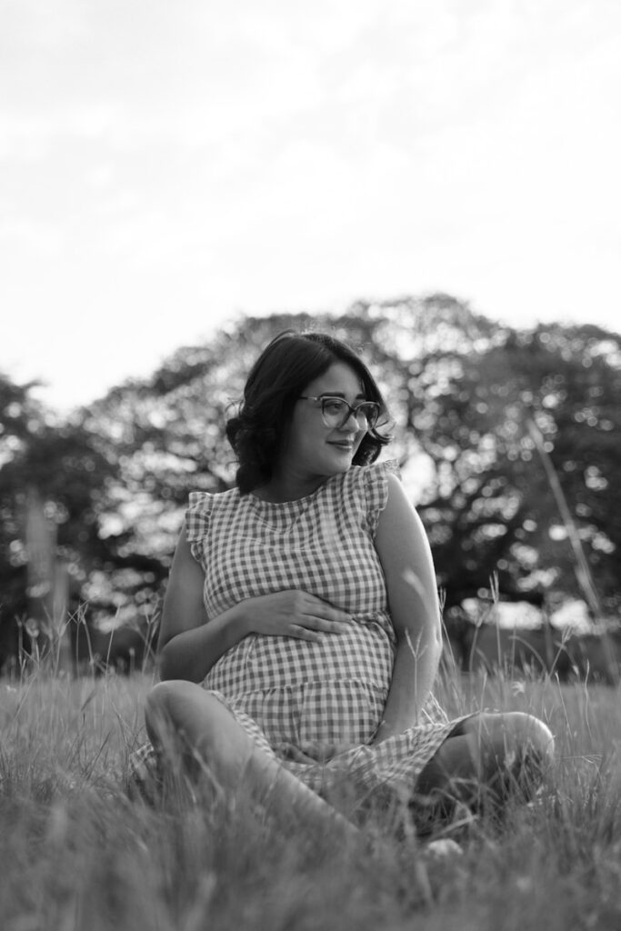 a pregnant woman sitting in a field talking on a cell phone